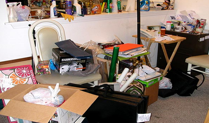 Cluttered living space filled with boxes, bags, and random items scattered around chairs and tables, creating a disorganized atmosphere.
